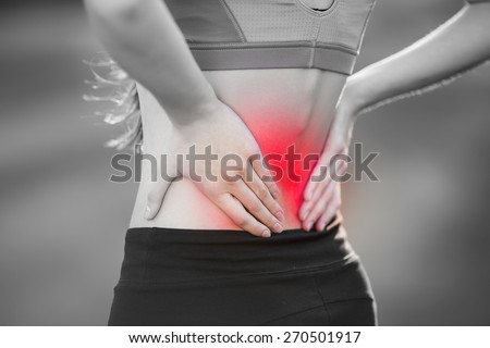 Back pain. Athletic woman in pink sportswear standing at the seaside rubbing the muscles of her lower back, cropped torso portrait.