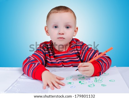 The boy draws a pencil at the table covered with a white tablecloth