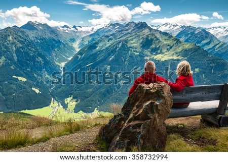 healthy and vital senior couple sitting on bench in austrian alps with beautiful view