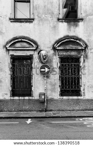 Black and white photo of an arrow traffic sign and a road mirror in an old Italian town