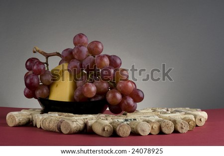 Wine cork with yellow cheese on black plate and red grape over grey background.