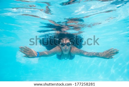 Woman swimming underwater in pool smiling. Young female swimmer with swim goggles at holiday resort