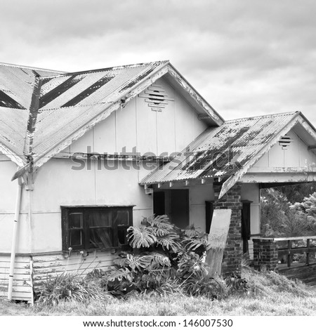 old abandoned farmhouse with rusted roof and neglected yard in black and white