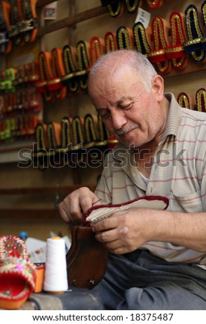 old man making colorful slippers for women