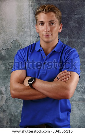 Young man stood wearing blue t-shirt with arms folded