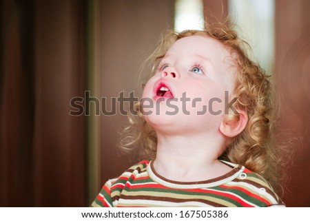Closeup portrait of preschooler with strawberry blonde curly hairs who lifts up her head