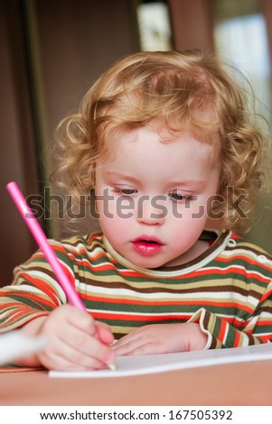 Closeup portrait of preschooler with strawberry blonde curly hairs who draws in the sketchbook by pencil and looks down