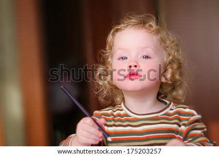 Closeup portrait of preschooler with strawberry blonde curly hairs who draws in the sketchbook by pencil and looks into the lens