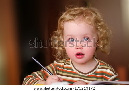Closeup portrait of preschooler with strawberry blonde curly hairs who draws in the sketchbook by pencil and looks up