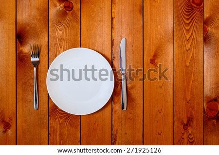Empty white round plate with antique knife and fork on wooden background. Top View with text space.