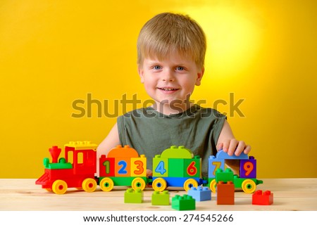Smiling kid playing with bricks on the table on yellow background. ?oncept of early learning.