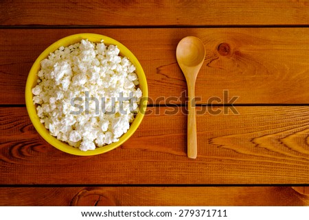 Cottage cheese in the yellow ceramic bowl and wooden spoon, top view