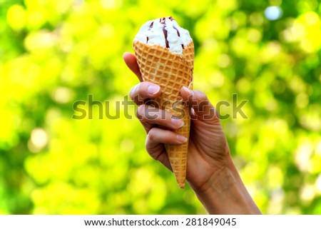 Cone ice cream in women's hand on natural green background