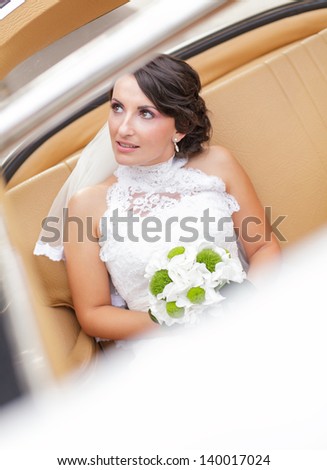 Bride on her wedding day in a vintage car with green bouquet
