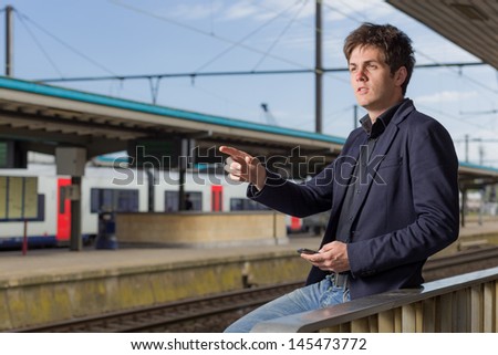 Young man in a train station pointing away and holding a smartphone