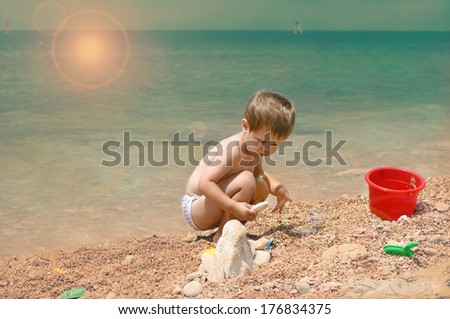 The child plays on the seashore.Toddler passionate about his game. Seashore, bucket, shovel and molds plus  great imagination and ability to play in the child.  Horizontal photo.