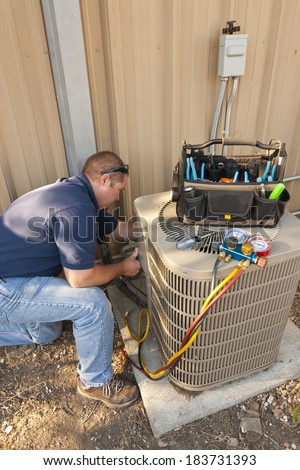 Air Conditioner Repair Man.  Using testing equipment on outside unit.  Tool bag on top of compressor.