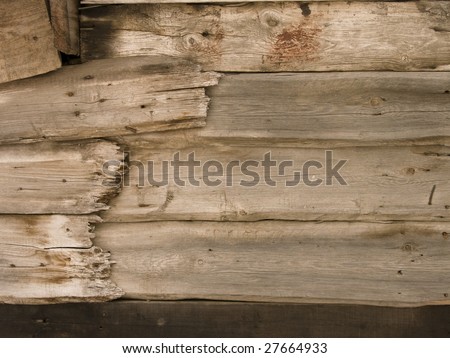 Closeup of an old wooden shed made of rough planks, with breaks, rusty nails\' heads, knots and a spot of reddish  paint