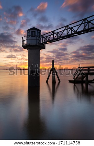 Dock pole and lighthouse at sunrise at Lauwersmeer