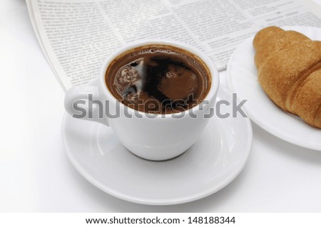 Cup of black coffee, croissants and breakfast accessories against a newspaper.