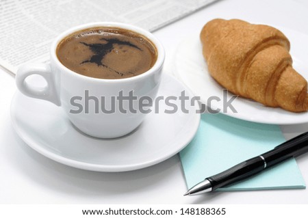 Cup of black coffee, croissants and breakfast accessories against a newspaper.