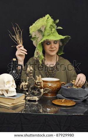 Magic woman in green hat with smoking twigs on black background