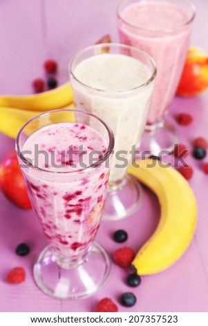 Milk cocktail with banana, blackcurrant and raspberry in a glass on purple wooden background