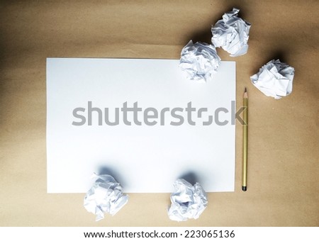 Crumpled up papers with a sheet of blank paper and a pencil on brown background