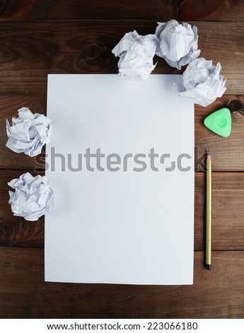 Crumpled up papers with a sheet of blank paper and a pencil on brown wooden background
