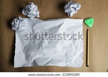 Crumpled up papers with a sheet of blank paper and a pencil on brown background