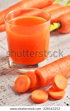 Glass of carrot juice and fresh carrots on white wooden background