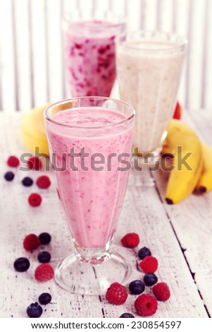 Milk cocktail with banana, blackcurrant and raspberry in a glass on white wooden background