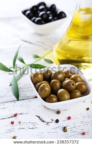 Green and black olives in bowl on white wooden background