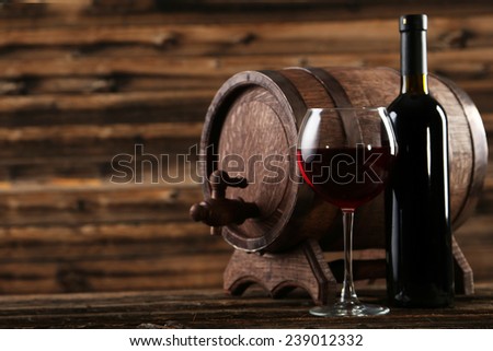 Red wine glass with bottle and barrel on brown wooden background