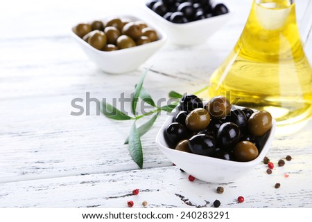 Green and black olives in bowl on white wooden background