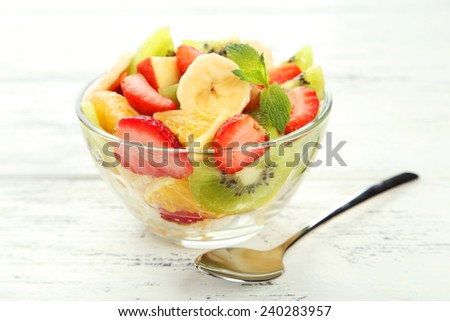 Fresh fruit salad in bowl on white wooden background
