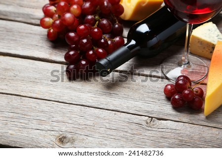Glass of red wine, cheeses and grapes on grey wooden background