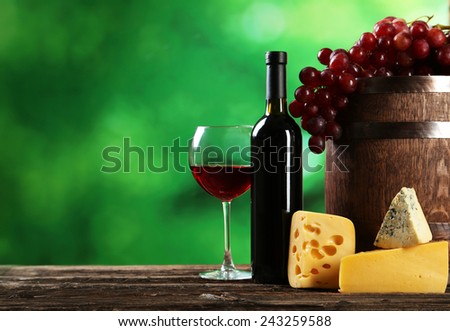 Glass of red wine, cheeses and grapes on brown wooden background