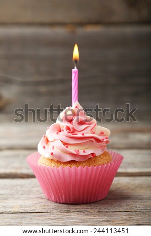 Tasty cupcake with candle on grey wooden background