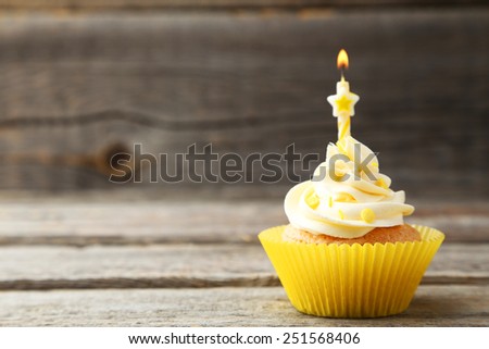 Tasty cupcake with candle on grey wooden background
