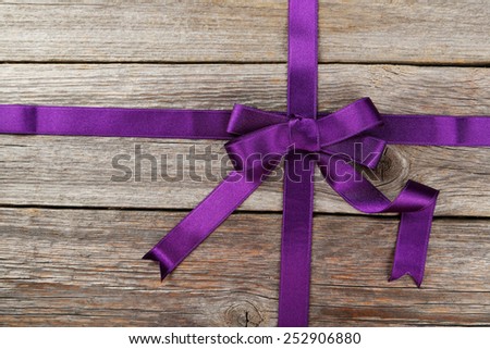 Purple ribbon with bow on grey wooden background