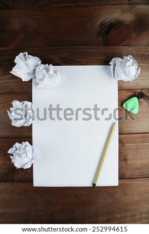 Crumpled up papers with a sheet of blank paper and a pencil on brown wooden background