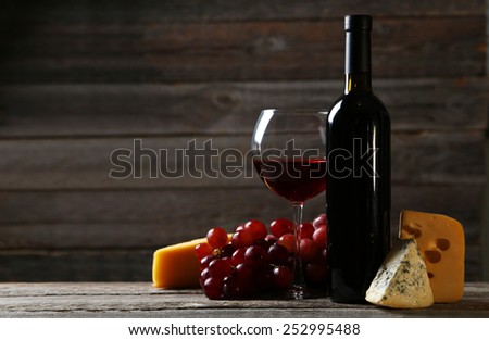 Glass of red wine, cheeses and grapes on grey wooden background