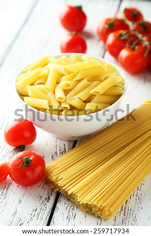 Spaghetti with bowl of pasta and tomatoes on white wooden background