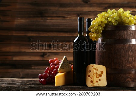 Bottles of wine, cheeses and grapes on brown wooden background
