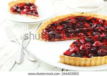 Fresh berry tart on plate on white wooden background