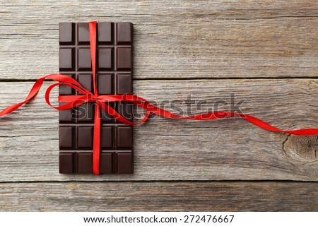 Dark chocolate bar with red bow on grey wooden background