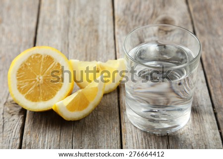 Lemons with glass of water on grey wooden background