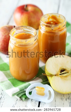 Jars of baby puree with apples on white wooden background
