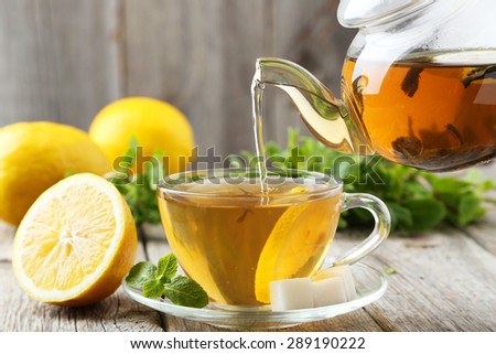 Pouring tea into cup of tea on grey wooden background